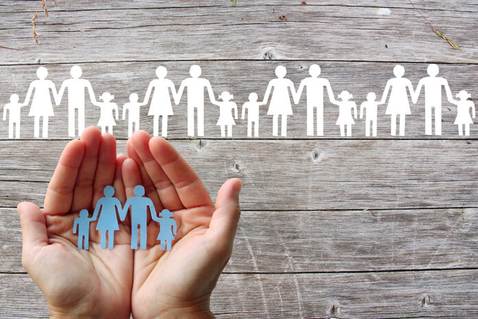 Paper family in hands on wooden background with white families